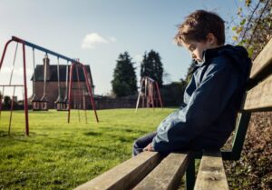 Kind sitzt allein auf einer Bank neben dem Spielplatz