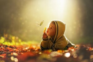 Kind liegt im Wald auf dem Boden und beobachtet einen Schmetterling