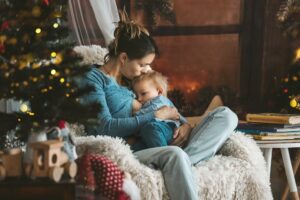 mutter stillt ihr baby in einem gemuetlichen sessel neben dem weihnachtsbaum