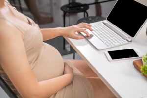 eine schwangere frau sitzt vor einem laptop