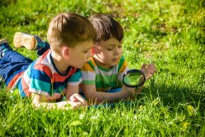 zwei Jungs liegen mit einer Lupe im Gras und erforschen die Umgebung